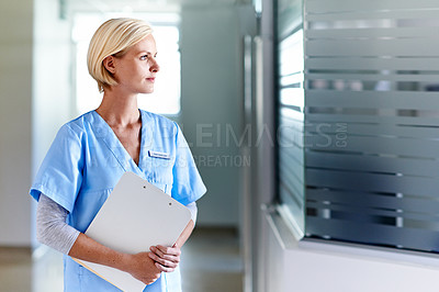 Buy stock photo Shot of a thoughtful-looking doctor standing in a hospital corridor