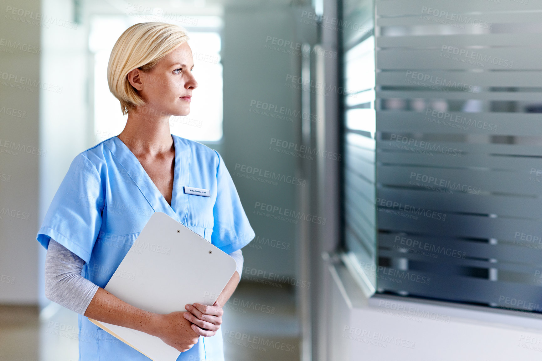 Buy stock photo Shot of a thoughtful-looking doctor standing in a hospital corridor