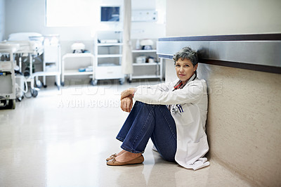 Buy stock photo Portrait of an exhausted doctor sitting in a hospital corridor