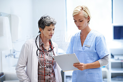 Buy stock photo Shot of two female doctors looking through a medical report together while standing in a ward