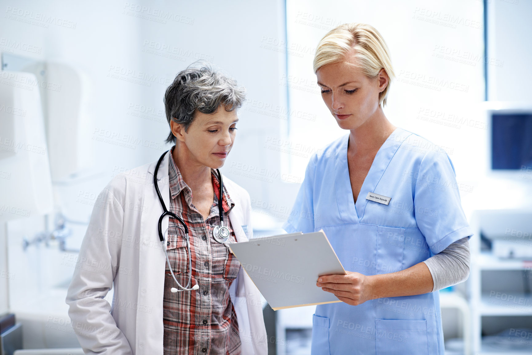 Buy stock photo Shot of two female doctors looking through a medical report together while standing in a ward