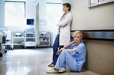 Buy stock photo Shot of two tired looking doctors in a hospital corridor