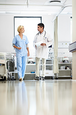 Buy stock photo Shot of two doctors walking down a hospital corridor