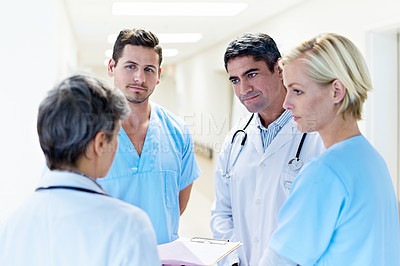 Buy stock photo Shot of a group of doctors looking through a medical report together while standing in a ward