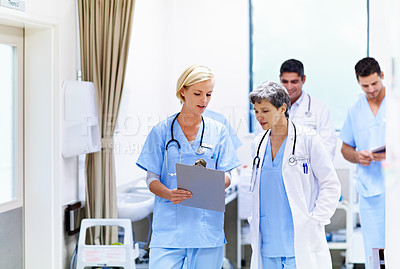 Buy stock photo Shot of a group of doctors looking through a medical report together while walking down in a ward