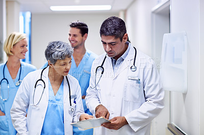 Buy stock photo Shot of a group of doctors looking through a medical report together while walking in hospital corridor