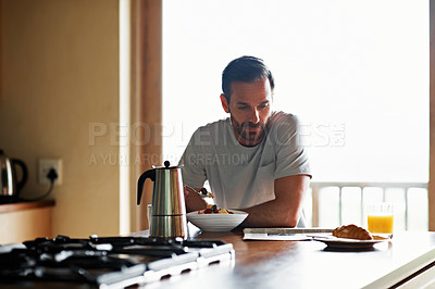 Buy stock photo Shot of a man eating his breakfast while reading a newspaper