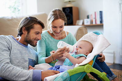 Buy stock photo Shot of a young couple feeding their baby at home