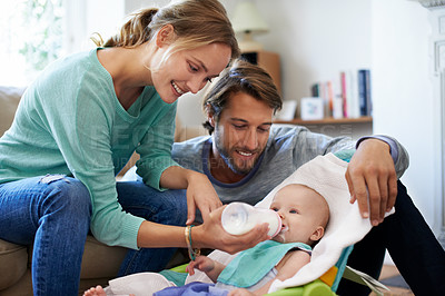Buy stock photo Shot of a young couple feeding their baby at home