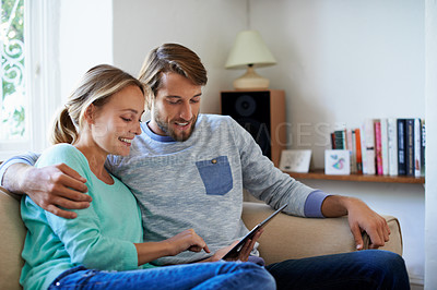 Buy stock photo Shot of a young couple using a digital tablet while relaxing on a sofa at home