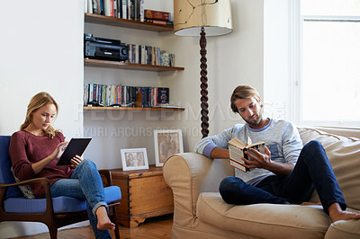 Buy stock photo Shot of a young couple relaxing with a book and digital tablet in the living room