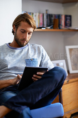 Buy stock photo Shot of a man using a digital tablet while relaxing at home