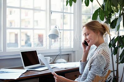 Buy stock photo Shot of a young woman talking on the phone while looking at paperwork