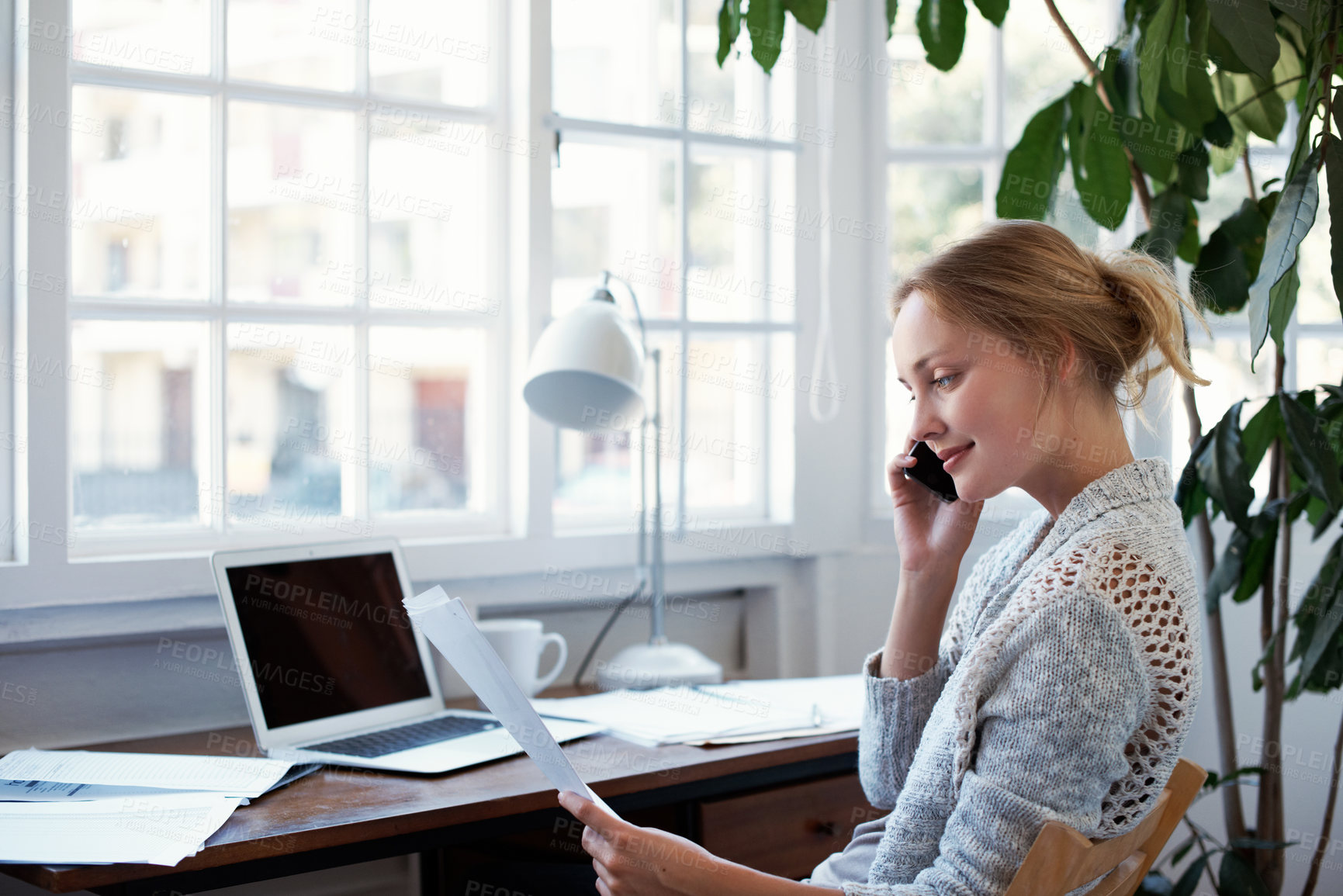 Buy stock photo Shot of a young woman talking on the phone while looking at paperwork