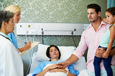 Buy stock photo Shot of doctors talking to a woman lying in a hospital bed while her husband and daughter look on