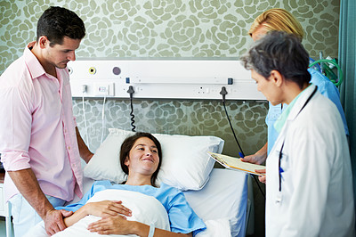 Buy stock photo Shot of doctors talking to a woman lying in a hospital bed while her husband looks on