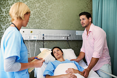 Buy stock photo Shot of a doctor talking to a woman lying in a hospital bed while her husband looks on