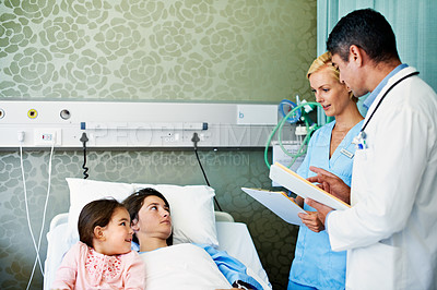 Buy stock photo Shot of doctors talking to a woman lying in a hospital bed with her daughter