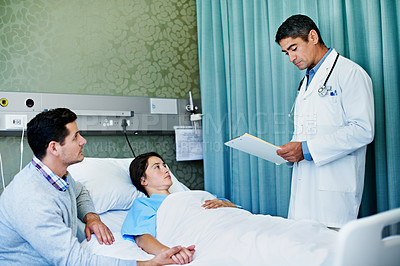 Buy stock photo Shot of a doctor talking to a woman lying in a hospital bed while her husband looks on