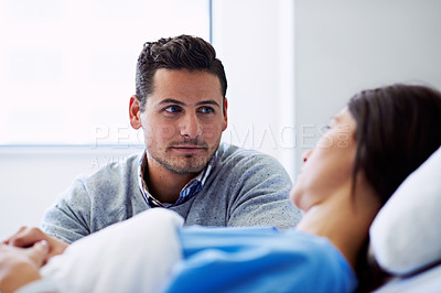 Buy stock photo Shot of a woman lying in a hospital bed being comforted by her husband