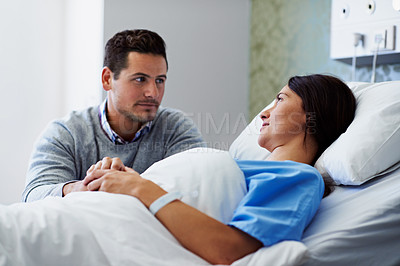 Buy stock photo Shot of a woman lying in a hospital bed being comforted by her husband