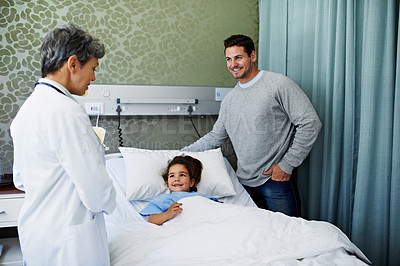 Buy stock photo Shot of a doctor talking to a little girl lying ing a hospital bed while her father looks on