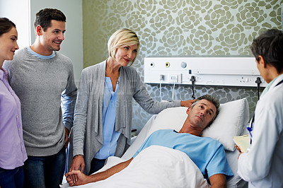 Buy stock photo Shot of doctors talking to a man in bed while his family looks on