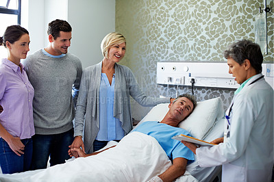 Buy stock photo Shot of doctors talking to a man in a hospital bed while his family looks on