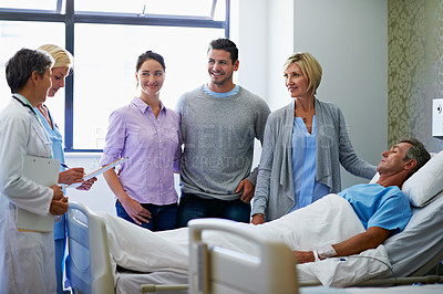 Buy stock photo Shot of doctors talking to a man in a hospital bed while his family looks on