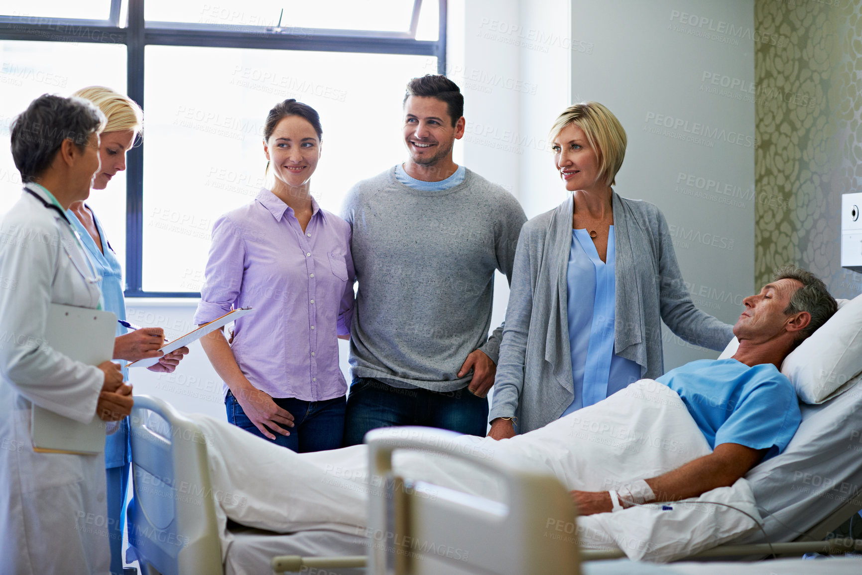 Buy stock photo Shot of doctors talking to a man in a hospital bed while his family looks on