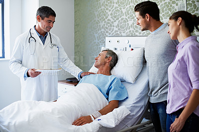 Buy stock photo Shot of a doctor talking to a man lying in a hospital bed while his adult children look on