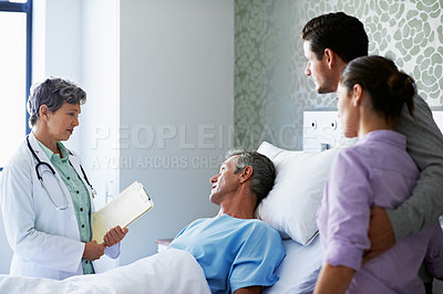 Buy stock photo Shot of a doctor talking to a man lying in a hospital bed while his adult children look on