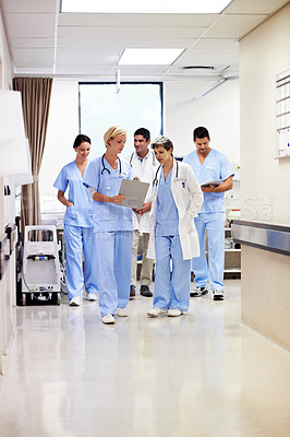 Buy stock photo Shot of a group of medical professionals walking down a hospital corridor