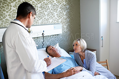 Buy stock photo Shot of a wife visiting her husband in the hospital while a doctor looks on
