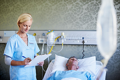 Buy stock photo Shot of a nurse reading a medical chart beside a patient in a hospital bed