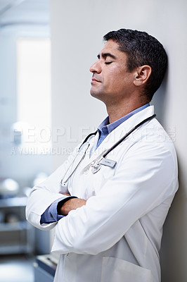 Buy stock photo Shot of a tired doctor leaning against the wall in a hospital