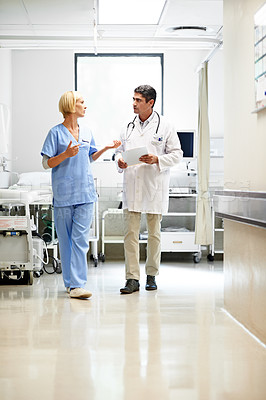 Buy stock photo Shot of two doctors walking down a hospital corridor
