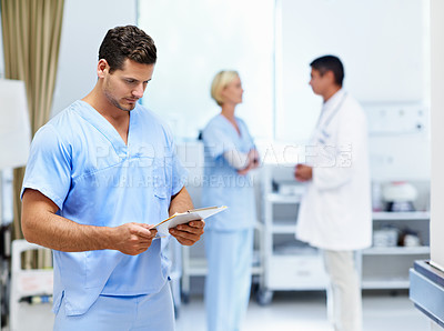 Buy stock photo Shot of a doctor looking through paperwork with colleagues in the background