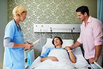 Buy stock photo Shot of a doctor talking to a woman lying in a hospital bed while her husband looks on