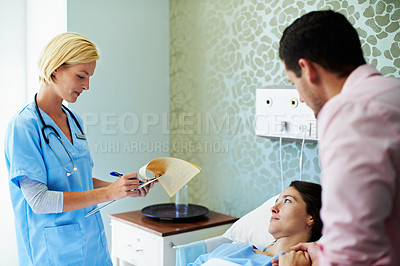 Buy stock photo Shot of a doctor talking to a woman lying in a hospital bed while her husband looks on