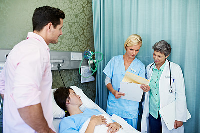 Buy stock photo Shot of doctors talking to a woman lying in a hospital bed while her husband looks on
