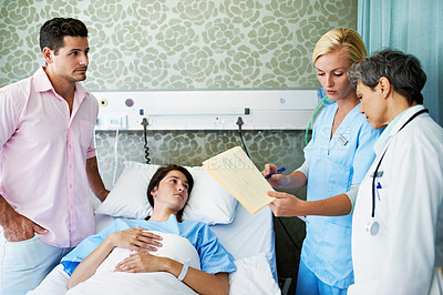 Buy stock photo Shot of doctors talking to a woman lying in a hospital bed while her husband looks on
