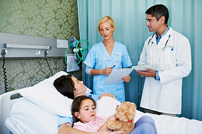 Buy stock photo Shot of doctors talking to a woman lying in a hospital bed with her daughter