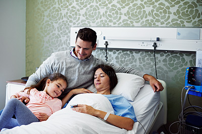 Buy stock photo Shot of a woman lying in a hospital bed with her husband and daughter beside her