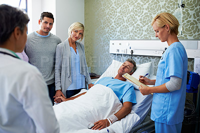 Buy stock photo Shot of doctors talking to a man in a hospital bed while his family looks on