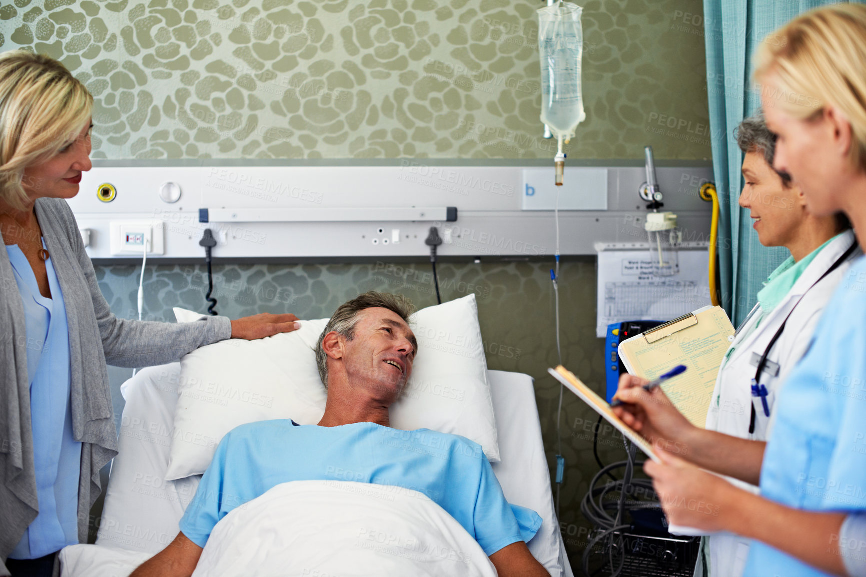 Buy stock photo Shot of a doctor talking to a man lying in a hospital bed with his wife beside him