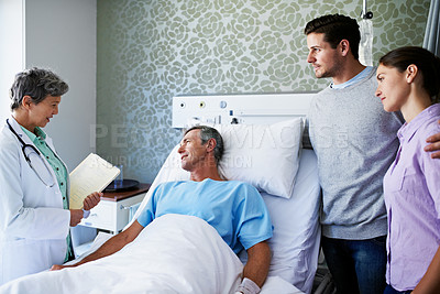 Buy stock photo Shot of a doctor talking to a man lying in a hospital bed while his adult children look on