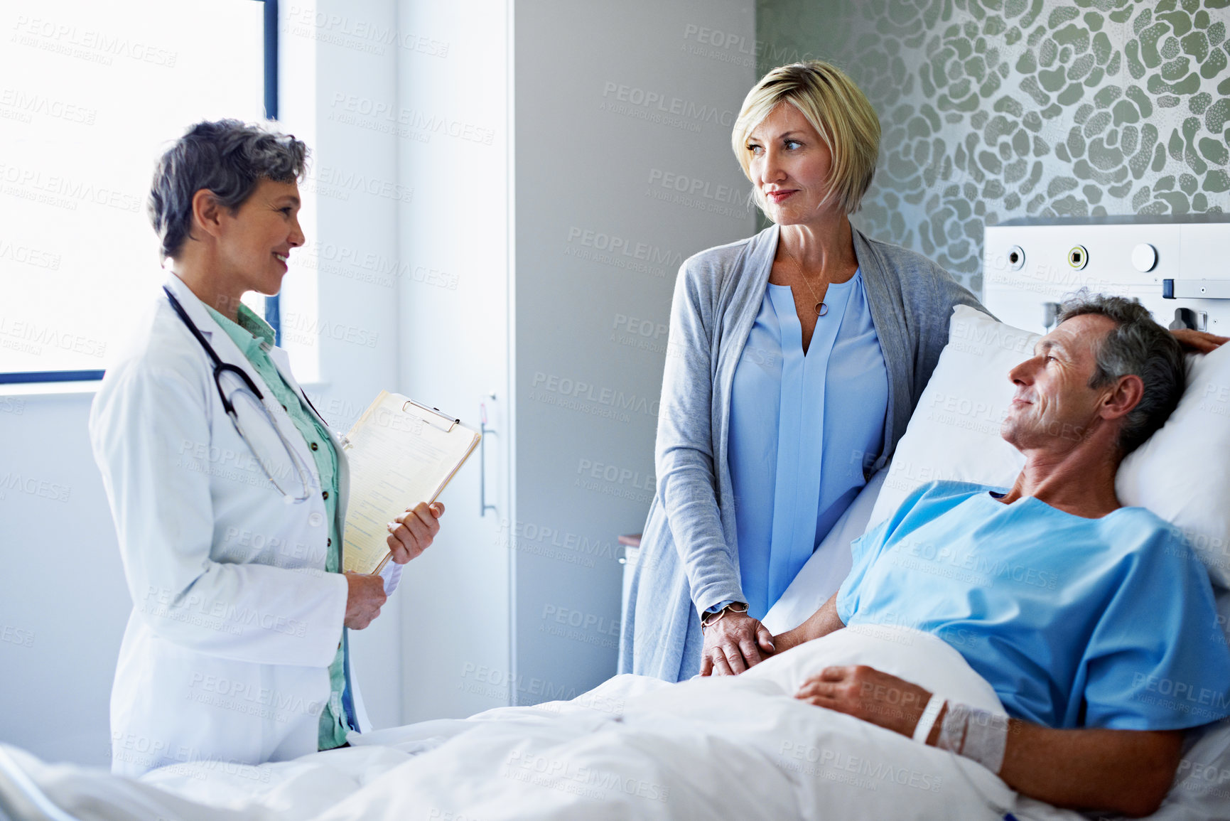 Buy stock photo Doctor, couple and monitoring patient in hospital bed for medical diagnosis, checkup or results. Healthcare worker, surgeon or discussion with man and woman for health recovery or treatment in clinic