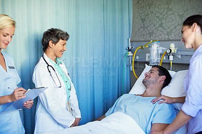 Buy stock photo Shot of doctors talking to a man lying in a hospital bed with his wife standing beside him