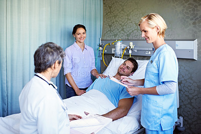 Buy stock photo Shot of doctors talking to a man lying in a hospital bed with his wife standing beside him